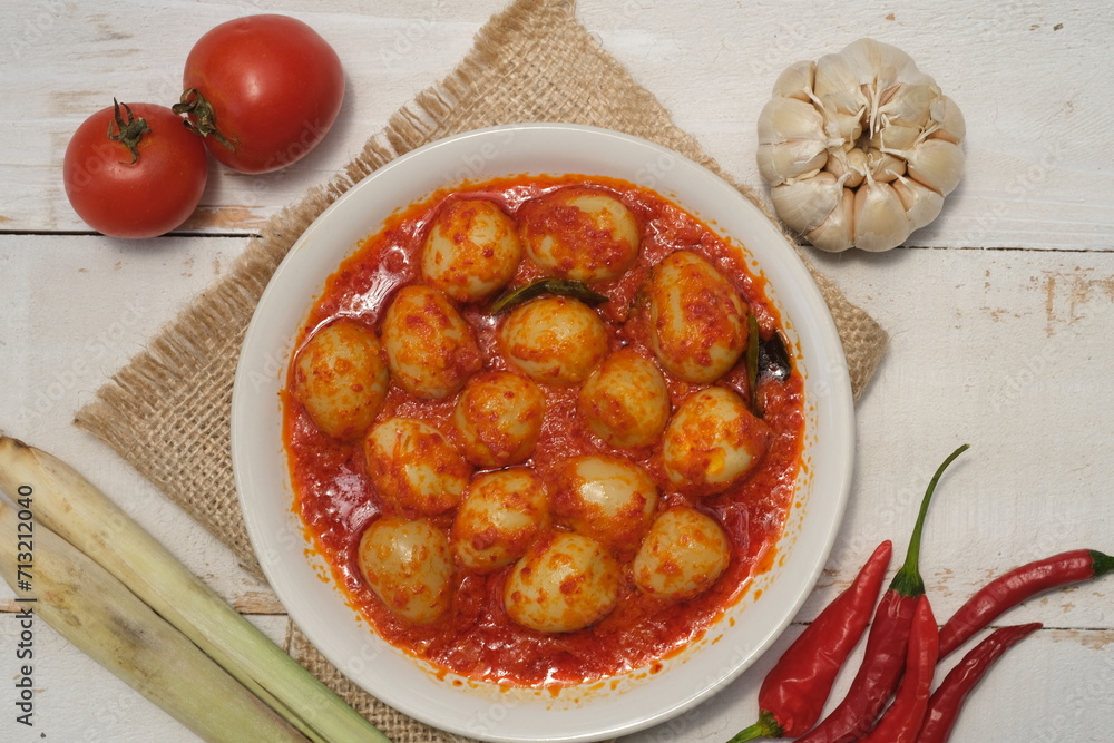 Telur Balado Tomat or Spicy Egg is traditional popular Indonesian food made from boiled egg with tomato and chili paste or sambal, served in white plate on wooden white table. Indonesian food. 
