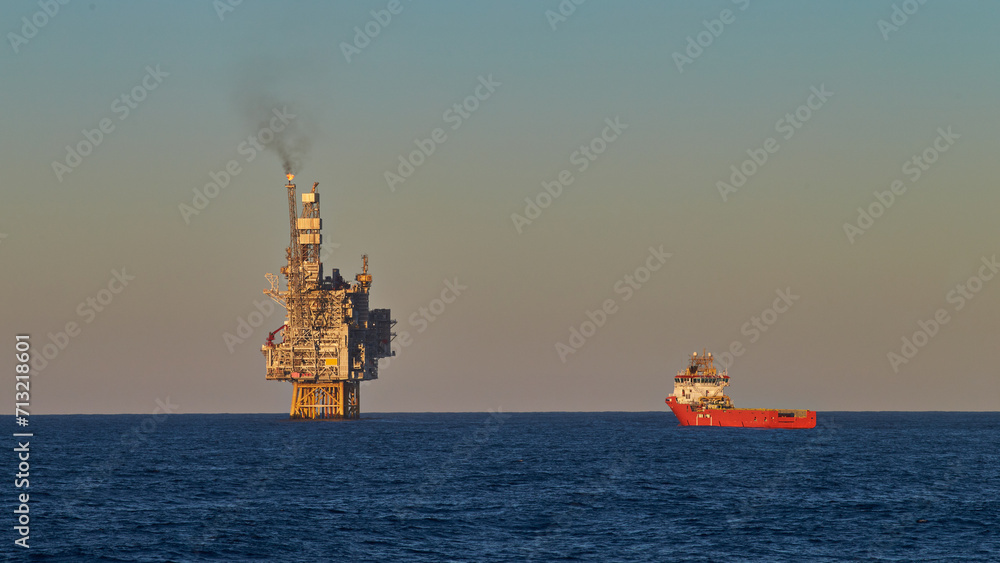 View of jack up drilling platform in the sea with supply vessel in fore ground. Oil and gas production in the sea.