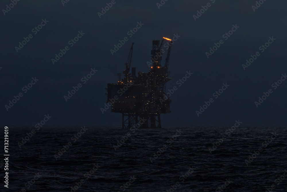 Picture of offshore oil and gas jackup drilling rig in the sea at night, with gas flare comming from pipe.