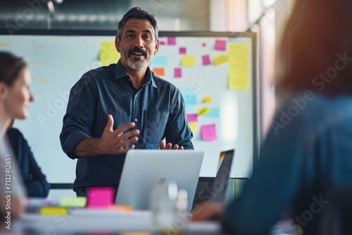 Latino man in his mid 40s confidently leading a team meeting with a laptop. business casual. large sunny board room with whiteboards and a few sticky notes for brainstorming. photo