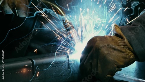 Close-up of a blacksmith welder working with metal using a welding machine, bright sparks and flashes in slow motion