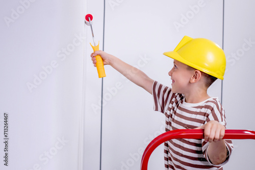 Child paints a wall with a roller. The boy is holding a large paint brush. House repair.