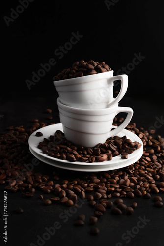 There are coffee beans in white cups and saucers on a dark background.