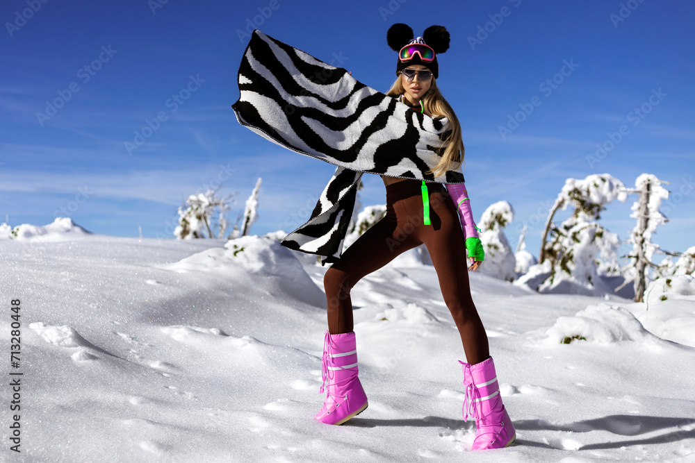 Beautiful woman wearing winter fashionable jacket and winter boots and is posing in the mountains.