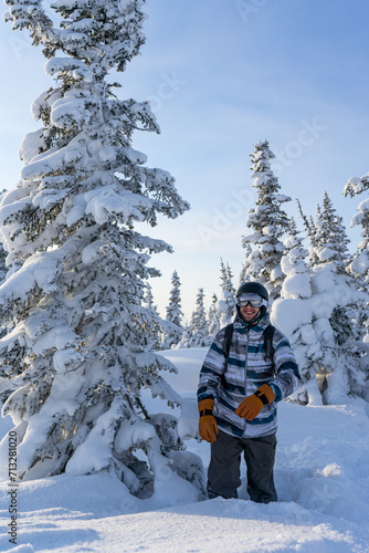 happy smiling man stands knee-deep in snow near a fluffy snow-covered tree. Person in equipment at ski resort