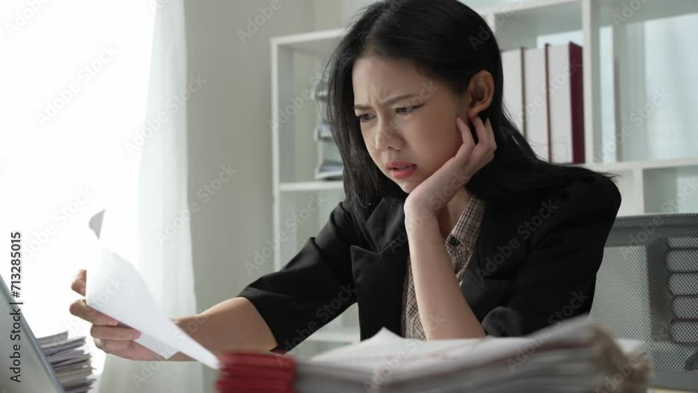 Tired Asian businesswoman reviews documents on table with broken financial data sheets, 4K Tired Asian businesswoman reviews documents on table with broken financial data sheets, 4K