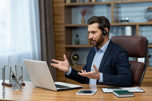 Mature businessman with headset engaged in an online conference call while working remotely from a home office setup.