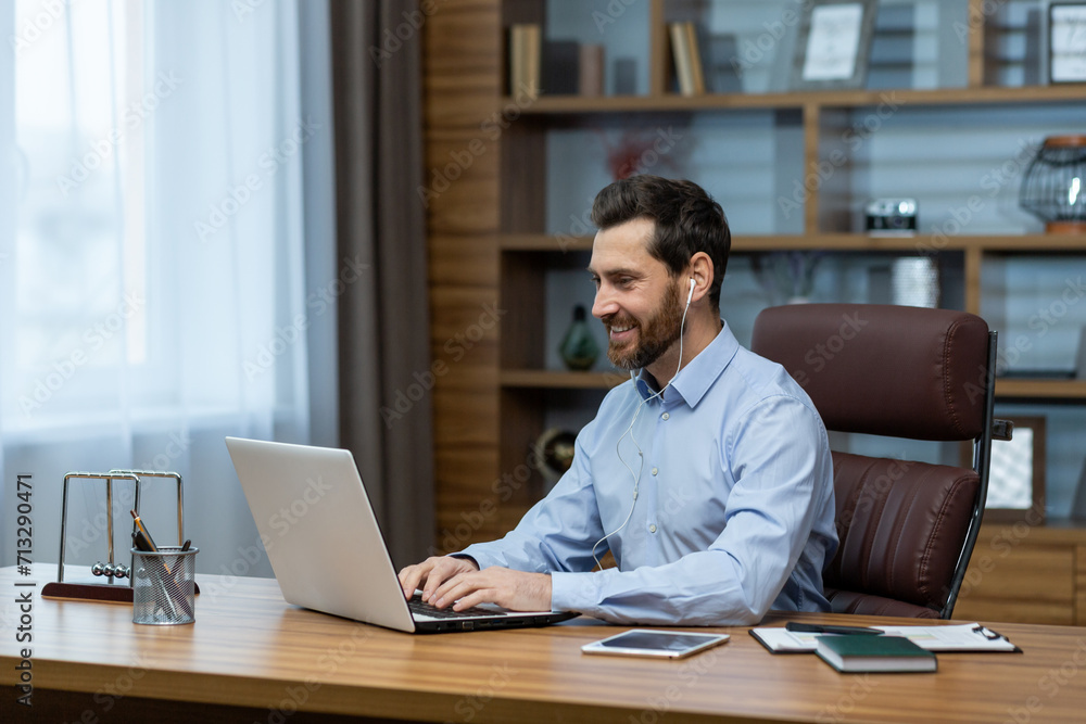 Obraz premium Smiling experienced male professional engaging in business via laptop at his home office setup, showcasing remote work.