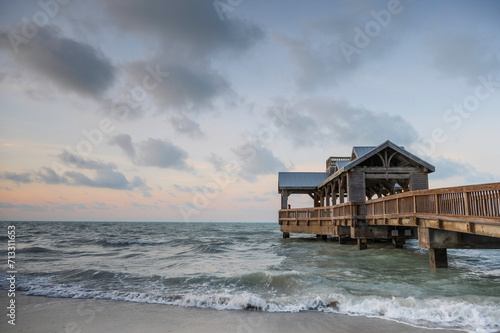 Wooden pier  with a covered open air structure at the end  reaching out into the tropical waters of the ocean  at sunrise. There is a hint of orange in the sky