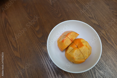 persimmon with skin removed and sliced to half on a white plate and wooden table