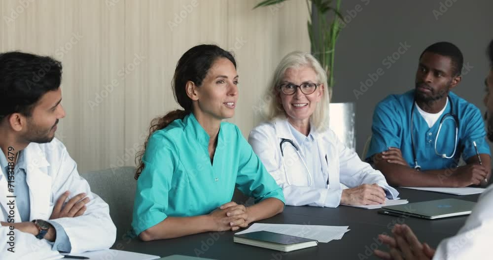 Happy young doctor woman in blue uniform offering ideas to colleagues for brainstorming, discussing medical occupation at professional meeting with diverse elder coworkers Happy young doctor woman in blue uniform offering ideas to colleagues for brainstorming, discussing medical occupation at professional meeting with diverse elder coworkers