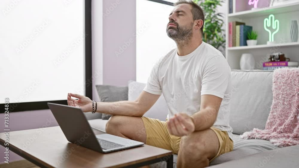 Mature hispanic man meditating indoors on a sofa with a laptop, showcasing modern home wellness. Mature hispanic man meditating indoors on a sofa with a laptop, showcasing modern home wellness.