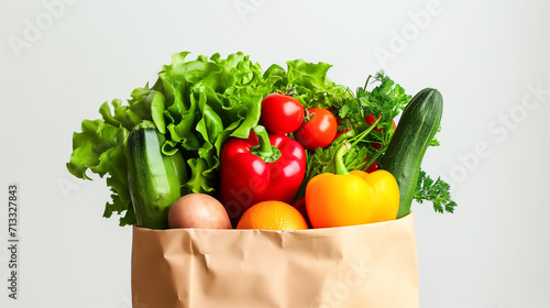 A brown paper bag filled to the brim with fresh produce, including green lettuce, red tomatoes, yellow bell pepper, zucchini, parsley and potatoes. Plain grey background.