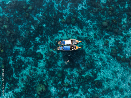 View from above, stunning aerial view of two long tail boats floating on a turquoise water while some tourists snorkel.  Phuket, Thailand. © Travel Wild