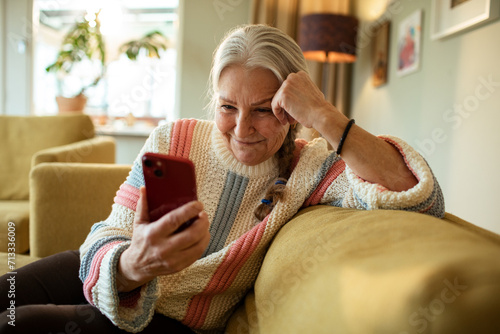 Smiling elderly woman using smartphone on home sofa photo