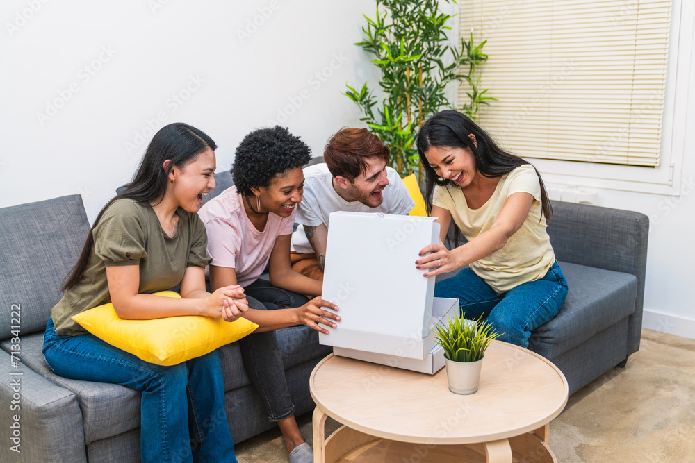 Fototapeta premium Diverse friends sharing the joy of opening a pizza box together in a comfortable living room, smiling and enjoying the moment
