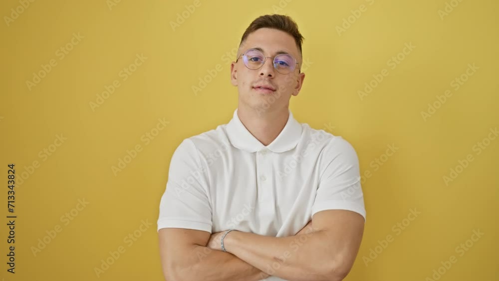 Radiant young hispanic man, wearing glasses and fashionably confident with crossed arms, flashes a friendly, successful smile. isolated yellow wall background Radiant young hispanic man, wearing glasses and fashionably confident with crossed arms, flashes a friendly, successful smile. isolated yellow wall background