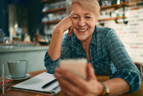 Senior woman smiling while using smartphone in kitchen