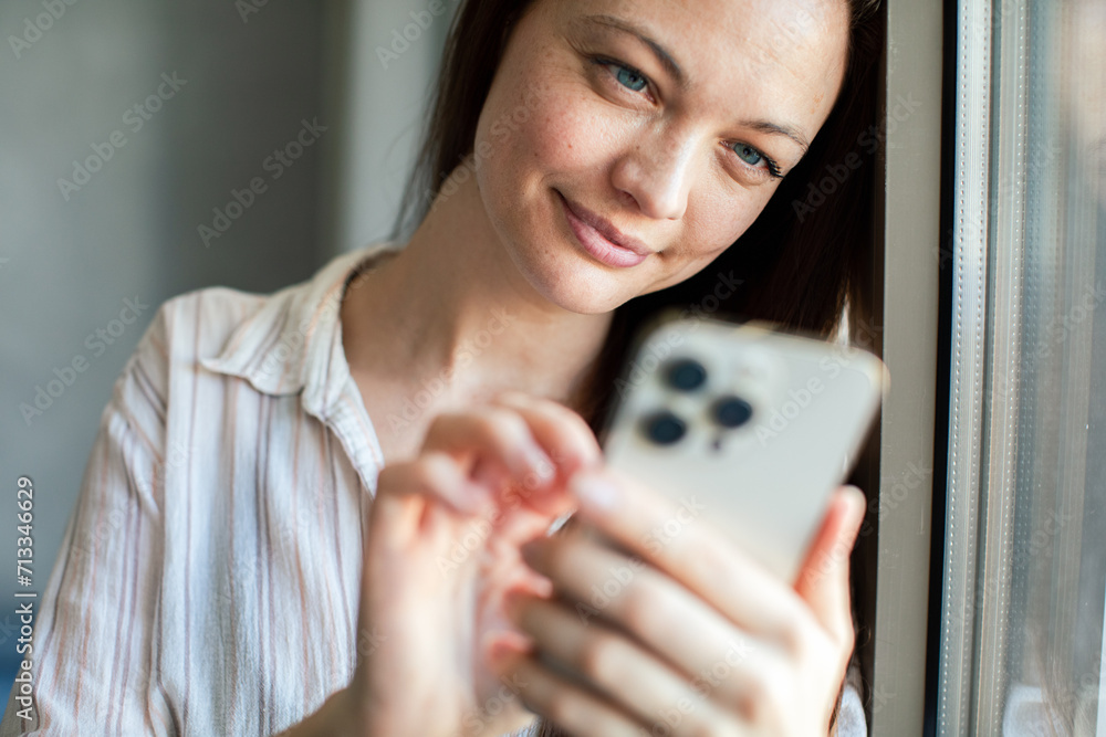 Close up woman using smartphone at home by window Close up woman using smartphone at home by window