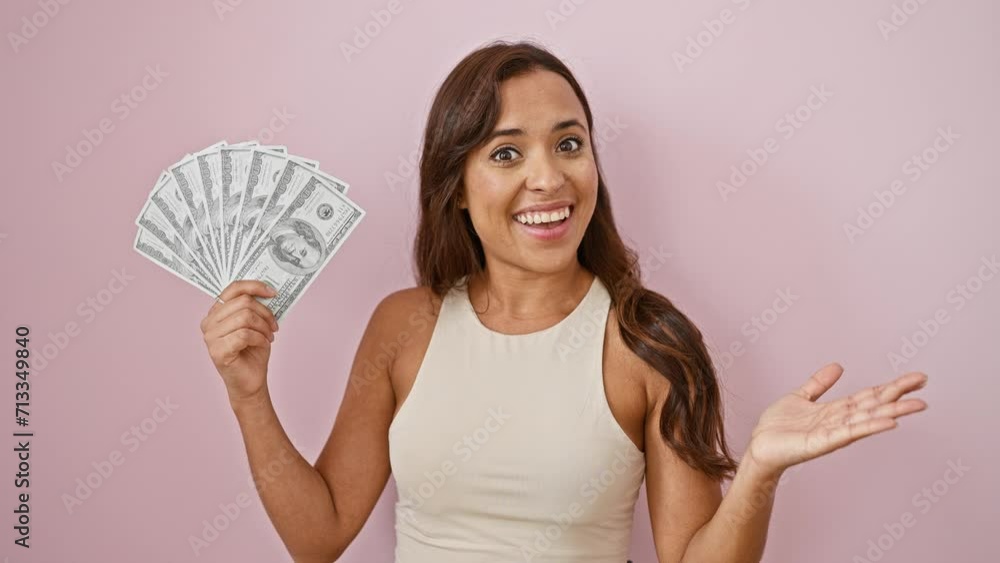 Triumphant young hispanic woman, victorious smile on her beautiful face, joyfully holding up dollar banknotes, celebrating a win, a success story against a striking isolated pink background. Triumphant young hispanic woman, victorious smile on her beautiful face, joyfully holding up dollar banknotes, celebrating a win, a success story against a striking isolated pink background.