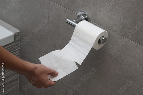 Close up of hand holding toilet paper roll in holder photo