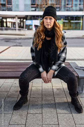 Woman in her mid-thirties with long red hair wearing a cap and black clothing in an urban location.