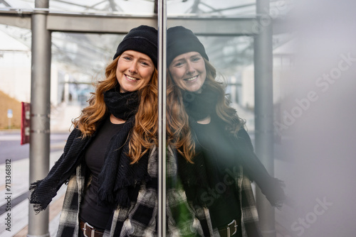 Woman in her mid-thirties with long red hair wearing a cap and black clothing in an urban location. photo