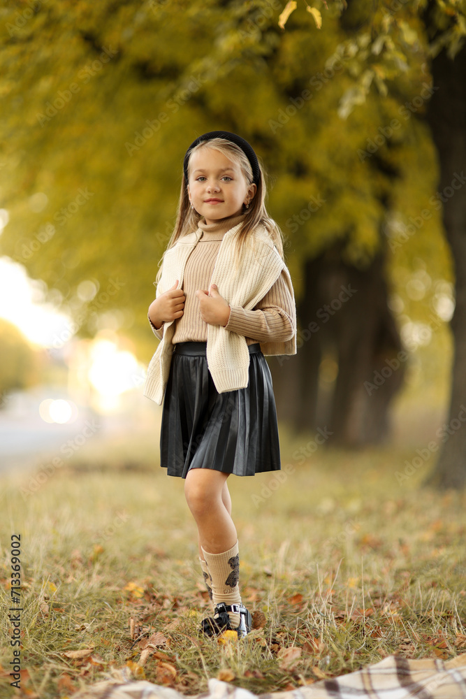 Children's day. Cheerful little child girl 5-6 years old posing and smiling at camera outdoors stand by the tree at autumn park. Stylish tender preschool kid wears beige knit sweater. Happy childhood. Children's day. Cheerful little child girl 5-6 years old posing and smiling at camera outdoors stand by the tree at autumn park. Stylish tender preschool kid wears beige knit sweater. Happy childhood.