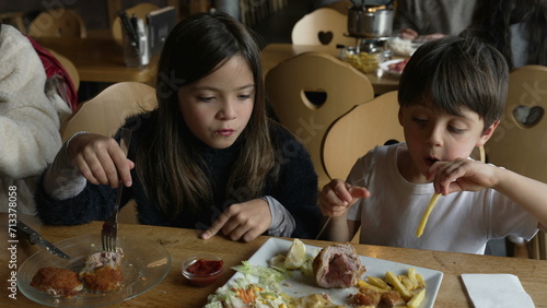 children enjoying mealtime at restaurant - small siblings, brother and sister interaction at diner eating food. Plate of milanese meat with fries