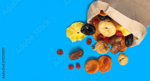 Different dried fruits in a paper bag on the blue background. Copy space. Top view.
