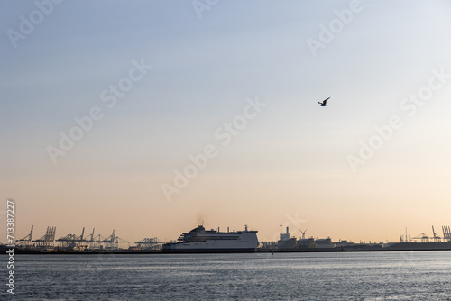 Ships float across the North Sea. Windmills in the background. Sea port in the Netherlands. A lot of cranes for loading goods. Different ships and barges.