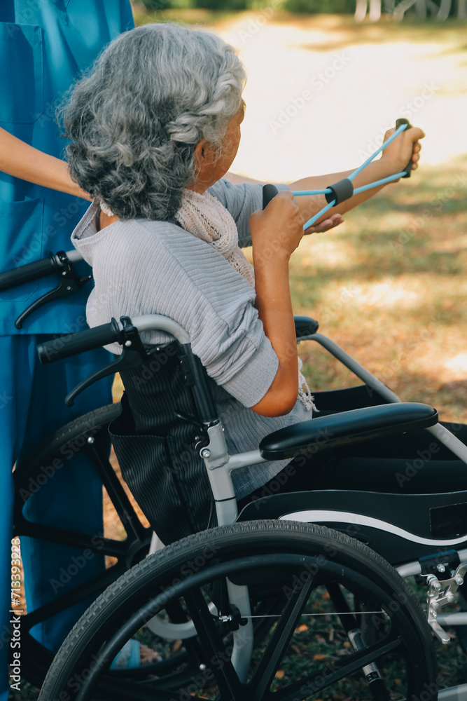 Obraz premium Young nurse or physiotherapist in scrubs helping a happy retired old woman do fitness exercises with light weight dumbbells at home. Concept of physiotherapy for seniors