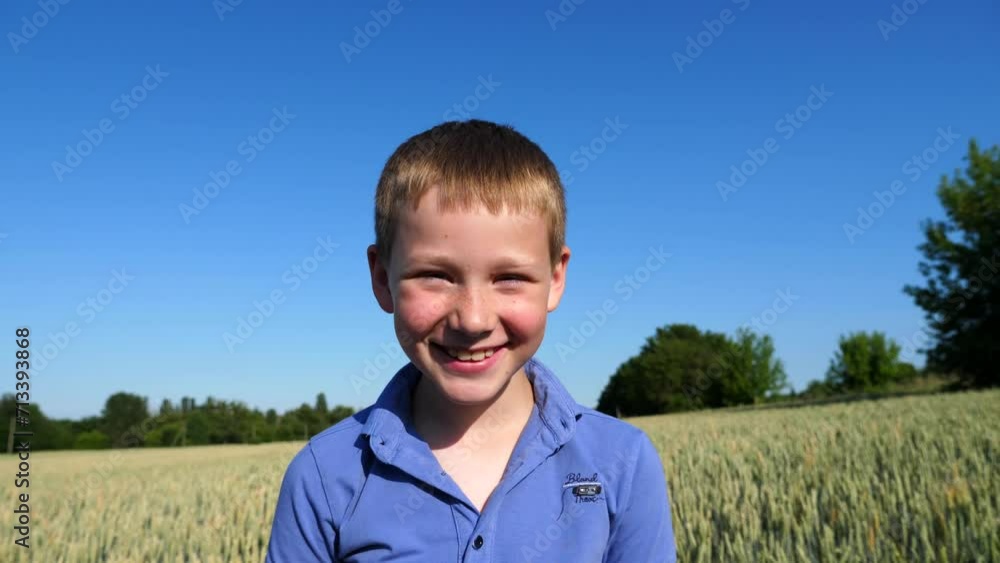 Little smiling boy with freckles looks into camera against background of wheat field. Portrait of happy child standing in barley meadow. Close up emotions of small kid with positive expression on face Little smiling boy with freckles looks into camera against background of wheat field. Portrait of happy child standing in barley meadow. Close up emotions of small kid with positive expression on face