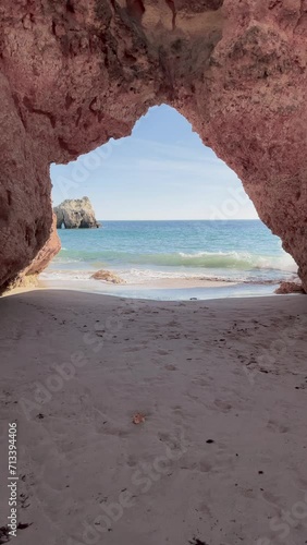 Waves crashing under an arch rock formation on a beach shore. 