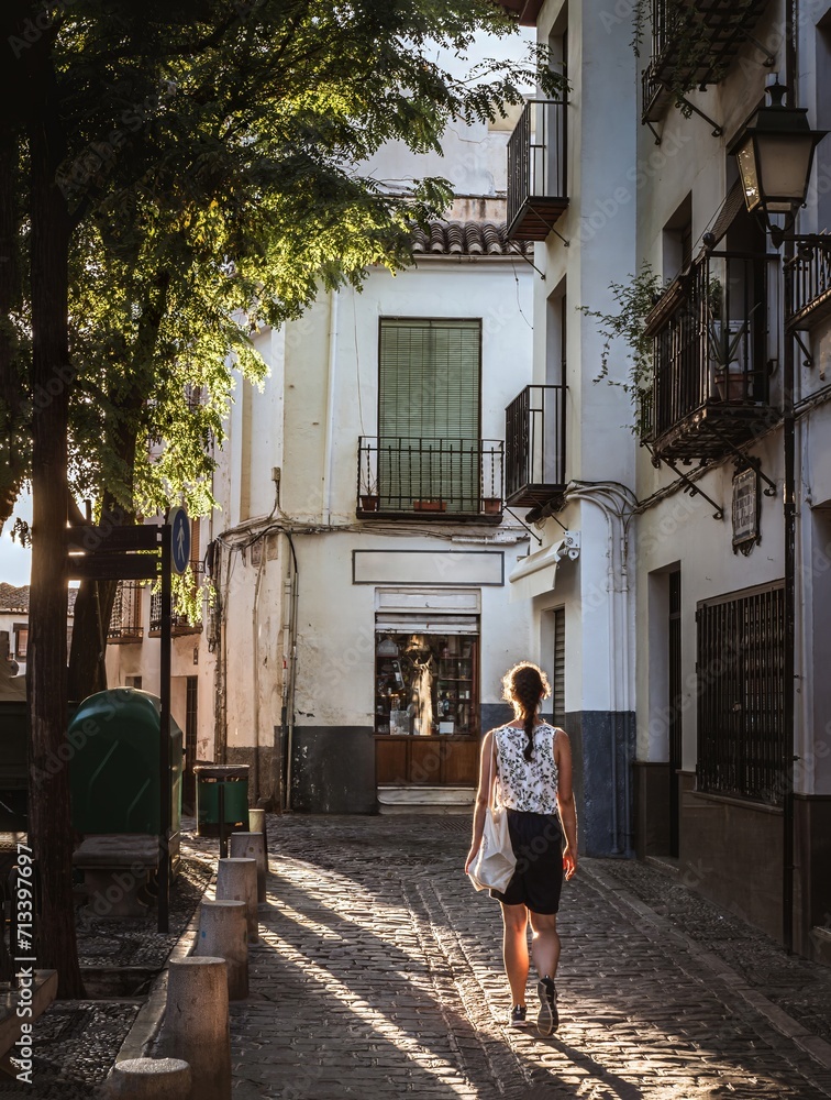 Young adult woman walking in sunlight in the Albaicin district of Granada, Andalusia, Spain