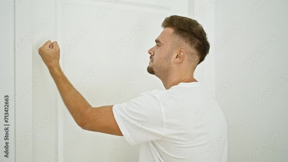 A young man knocks and pushes against a white door in a bright home interior. A young man knocks and pushes against a white door in a bright home interior.