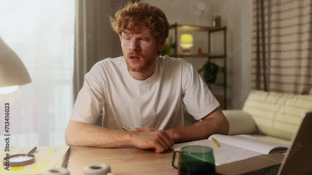 Unhappy young red haired man feeling annoyed when getting message on smartphone at home workplace Nervous male having problem on study or work conflict online indoors Unhappy young red haired man feeling annoyed when getting message on smartphone at home workplace Nervous male having problem on study or work conflict online indoors