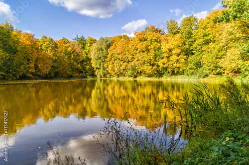 Landscape with Small lake in autumn forest, reflection on water, under blue sky.