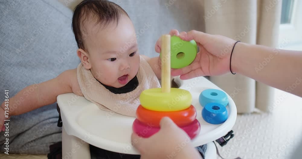 Joyful infant baby sits in a high chair learning to stack colorful rings with help from mother, a moment engaging in early childhood development activities. Joyful infant baby sits in a high chair learning to stack colorful rings with help from mother, a moment engaging in early childhood development activities.