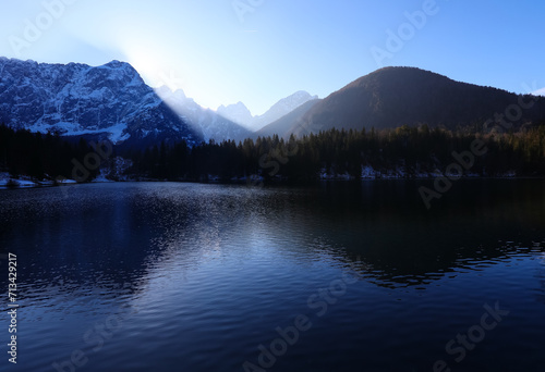 sun coming out behind the mountains and the reflection of the mountains on the beautiful alpine lake in winter