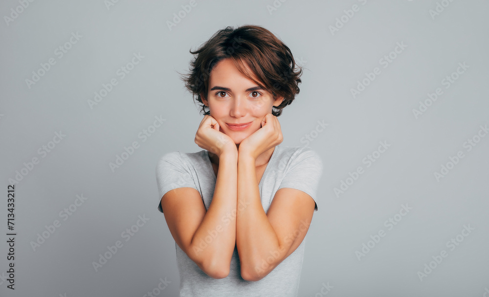 Close up portrait of cute tender gorgeous young woman with short curly hair in gray t-shirt. Girl looks straight on camera isolated in studio Close up portrait of cute tender gorgeous young woman with short curly hair in gray t-shirt. Girl looks straight on camera isolated in studio