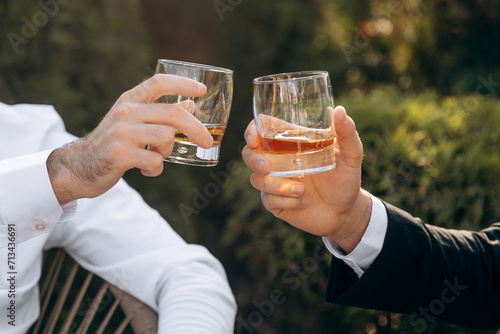 Close-up of hands with clinking whiskey glasses. Cheers mate