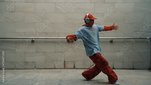 Handsome choreographer practice street dance in gray background. Young attractive b-boy dancer perform while wearing stylish cloth. Feeling of lively step. Copy space. Outdoor sport 2024. Sprightly.