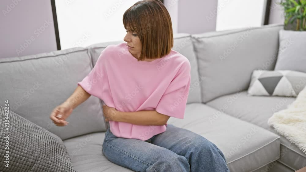 Worried, young hispanic woman suffering from a serious stomachache, resting uneasy on comfy sofa at home, hugging a cushion with a pained expression. Worried, young hispanic woman suffering from a serious stomachache, resting uneasy on comfy sofa at home, hugging a cushion with a pained expression.
