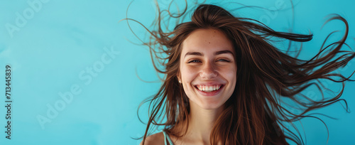 Smiling young pretty woman with brunette brown long groomed hair isolated on flat blue background with copy space. Perfect hair care products banner template, hair salon. photo