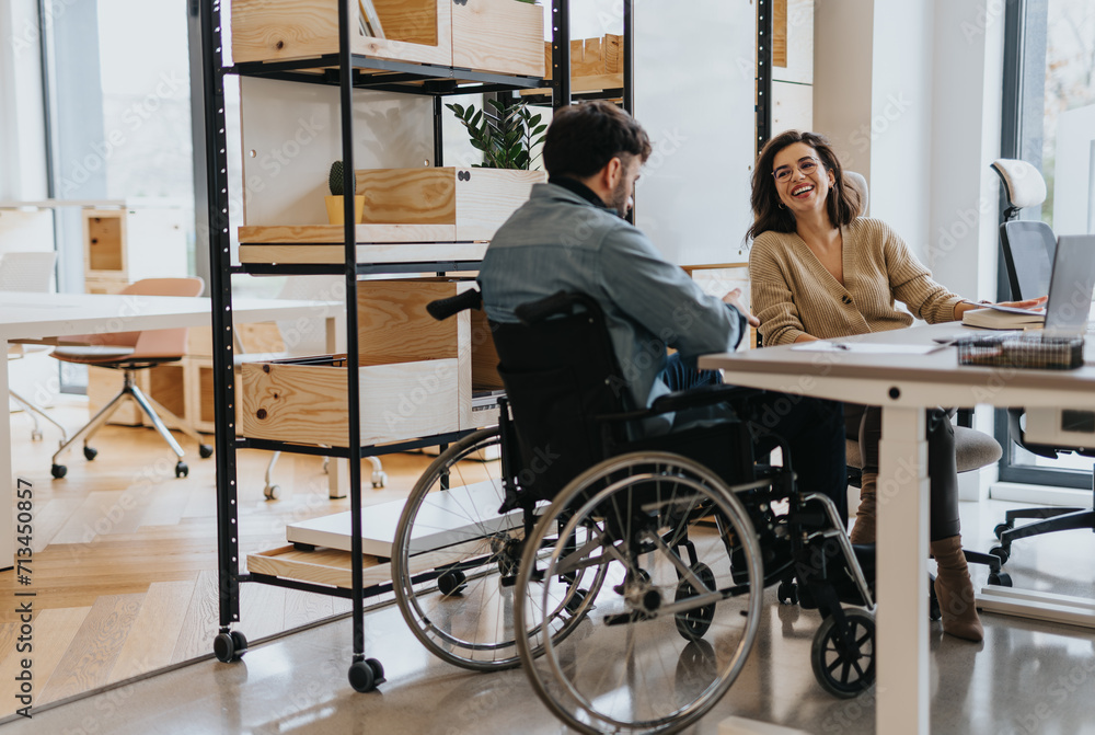 Successful woman discussing work with her handicapped male colleague in wheelchair at modern creative office. Successful woman discussing work with her handicapped male colleague in wheelchair at modern creative office.