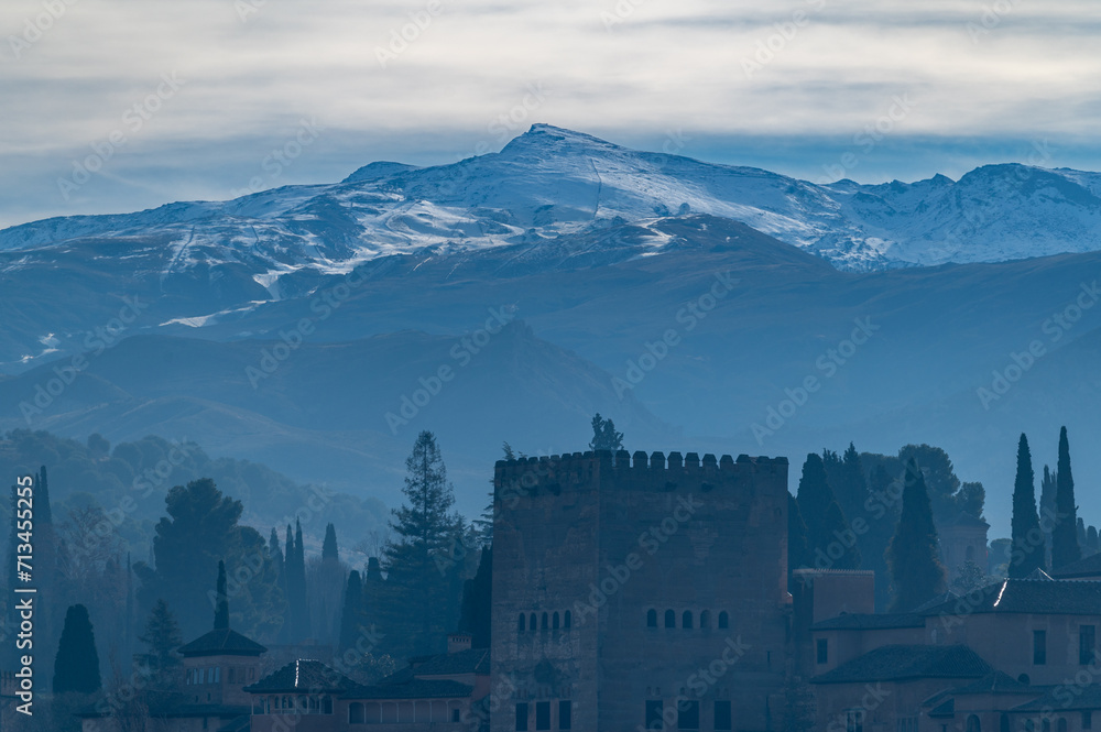 View of the towers of the Alhambra on a misty winter dawn with the snow-capped peaks of the Sierra Nevada in the background
