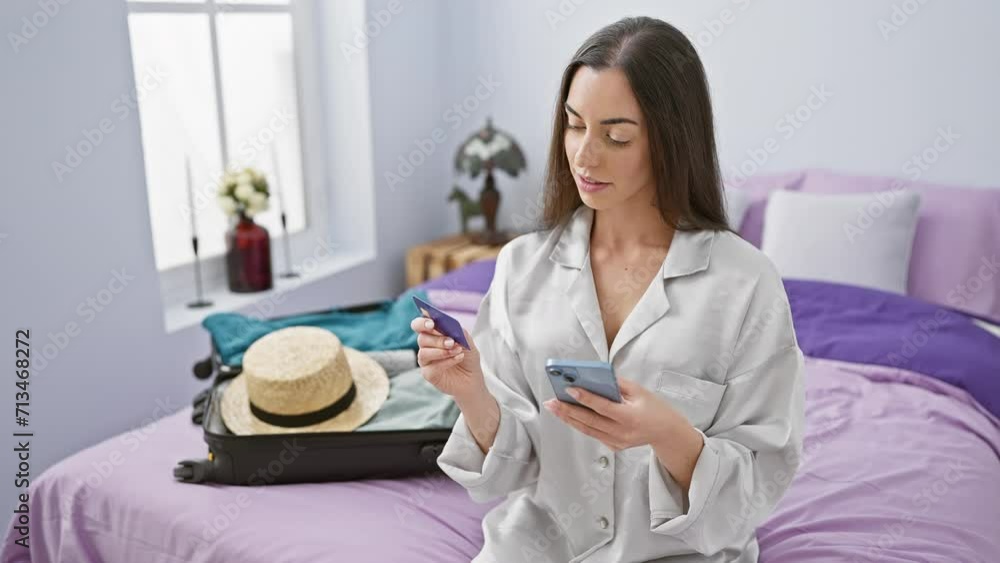 Cheerful young hispanic woman basking in the morning sunlight, snuggled in her hotel bed, joyfully shopping for her holiday journey using smartphone and credit card, suitcase ready for vacation. Cheerful young hispanic woman basking in the morning sunlight, snuggled in her hotel bed, joyfully shopping for her holiday journey using smartphone and credit card, suitcase ready for vacation.