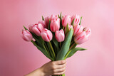 Beautiful bouquet of tulips in hand on a pink background