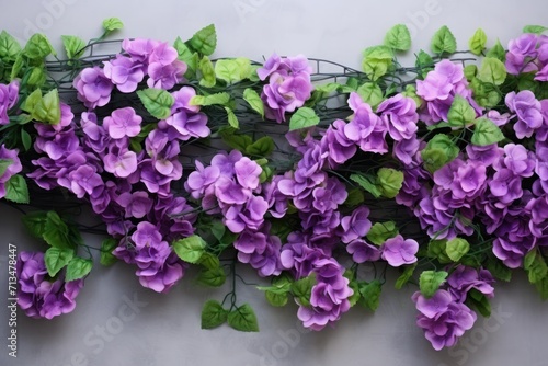  a bunch of purple flowers with green leaves on a white wall and a wire fence with green leaves on it.